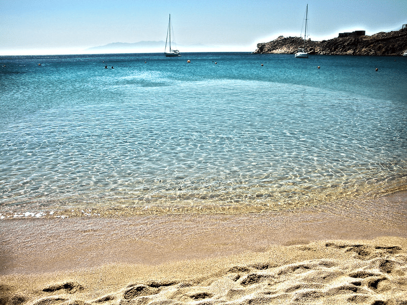 Wo soll man in Mykonos am Strand oder in der Stadt übernachten? Ein Blick auf die weißen/gelben Sandstrände von Mykonos mit dem perfekten blauen Wasser.