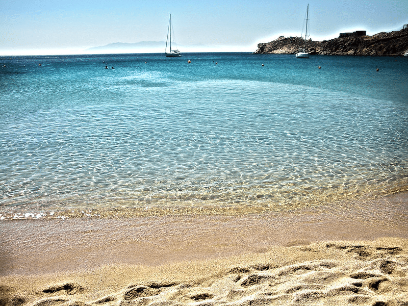 Where to stay in Mykonos beach or town? A view of the white/yellow sandy beaches of Mykonos with the perfect blue waters.